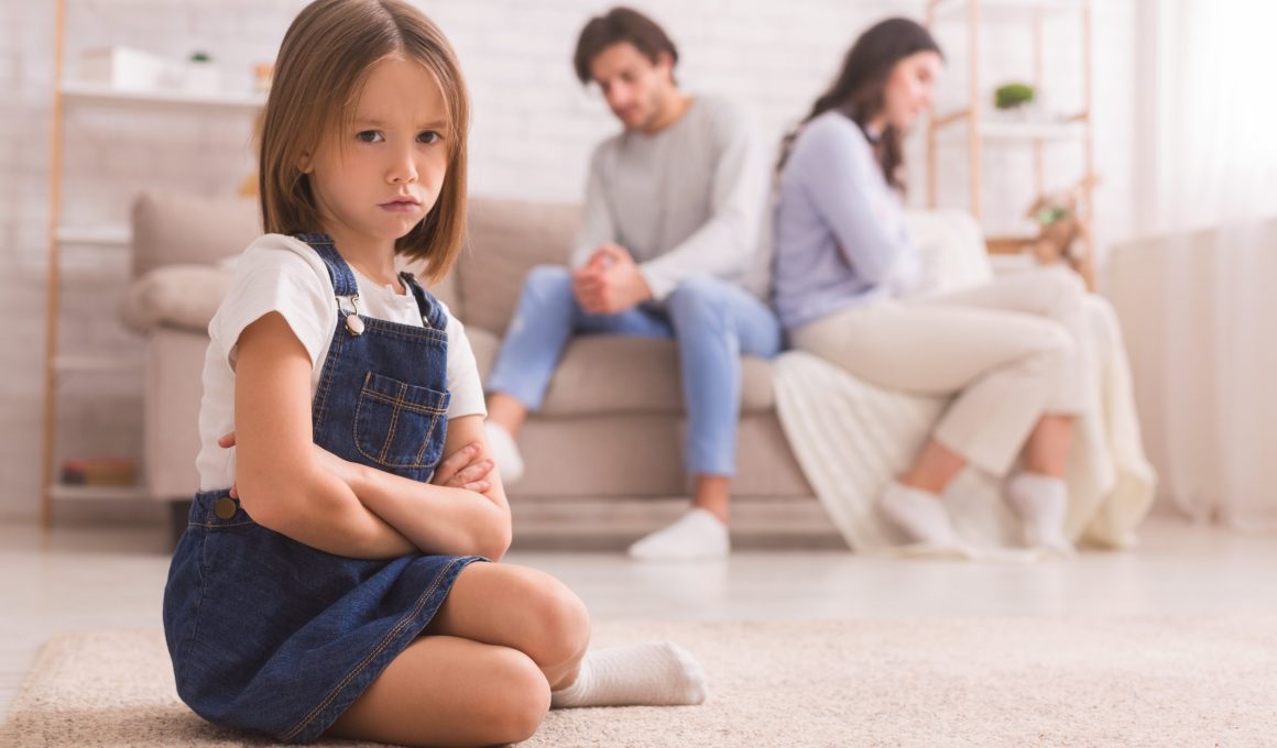 little girl frowning while unhappy couple sits on the couch
