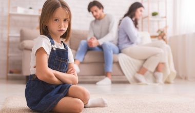 little girl frowning while unhappy couple sits on the couch