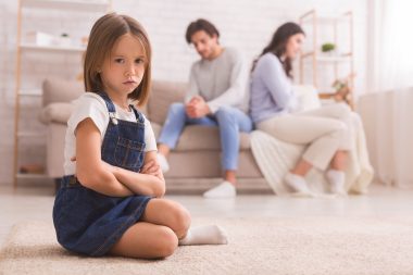 little girl frowning while unhappy couple sits on the couch