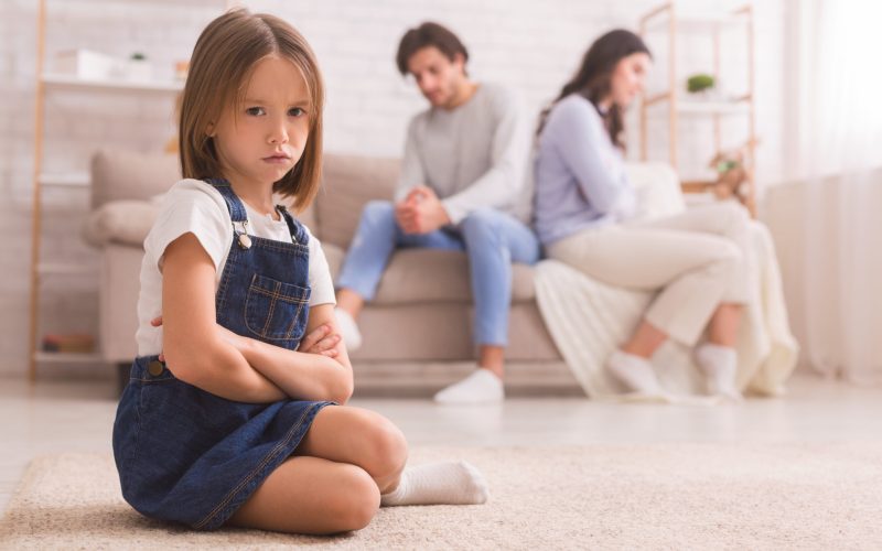 little girl frowning while unhappy couple sits on the couch
