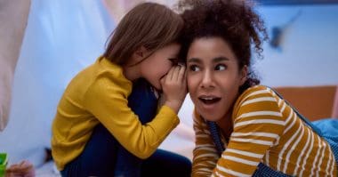 little girl whispering something on a woman's ear
