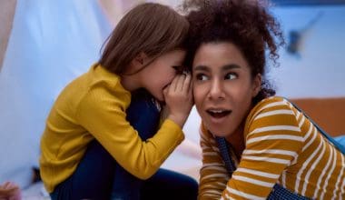little girl whispering something on a woman's ear