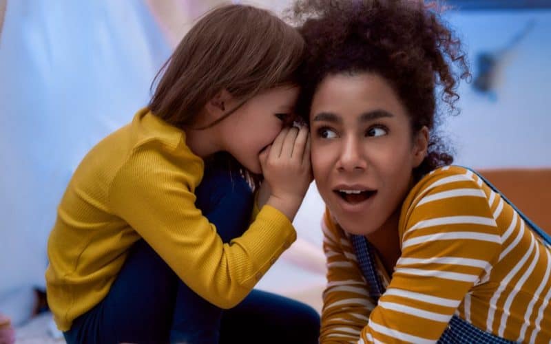 little girl whispering something on a woman's ear