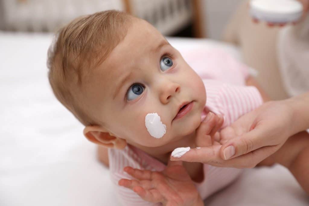 mother putting lotion on baby