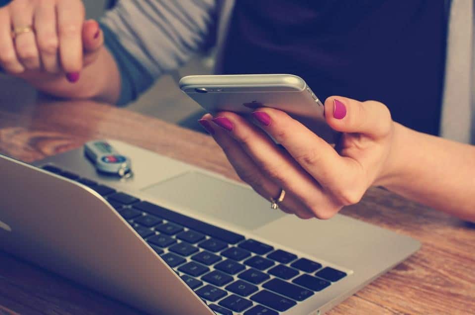 woman checking her phone while working on laptop