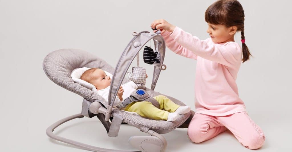 baby laying down in a cradle with her sister