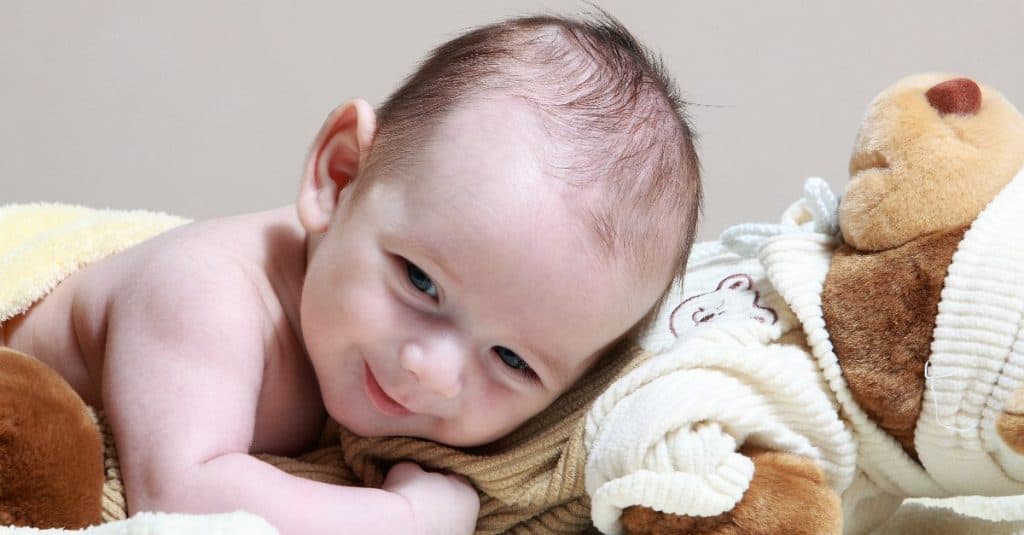 baby smiling and lying on his teddy bear