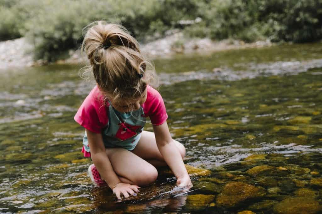 little girl playing with stones in a river