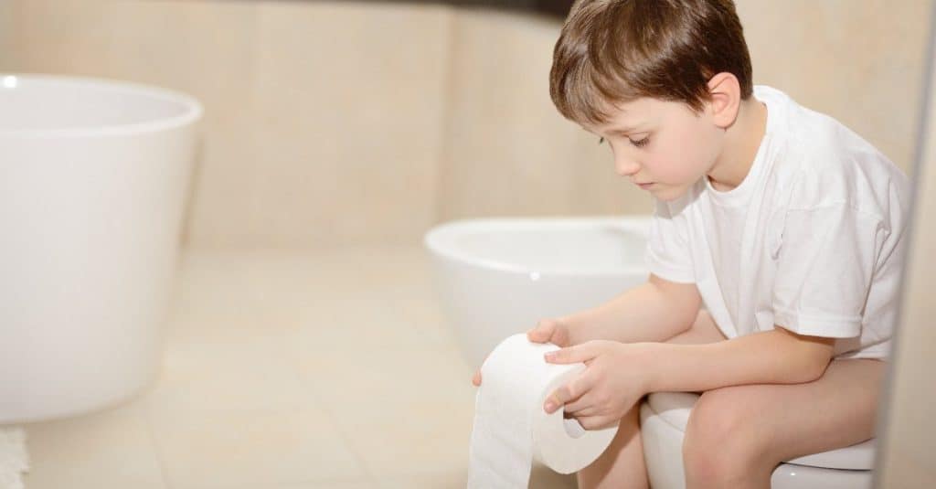 toddler sitting on toilet while holding toilet paper
