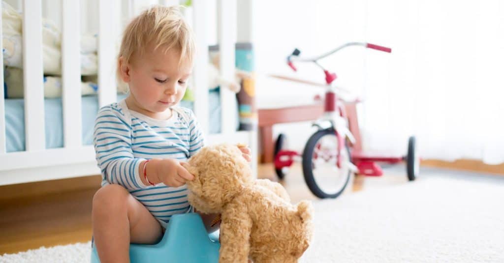 toddler using potty while playing with teddy bear
