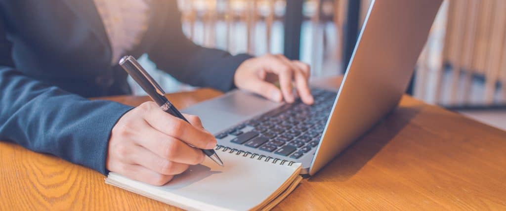 woman taking notes while on laptop