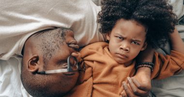 father and frowning kid on bed