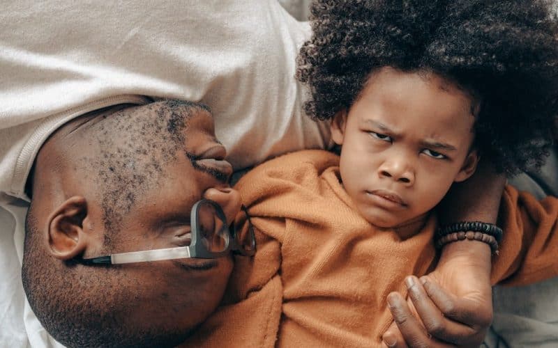 father and frowning kid on bed