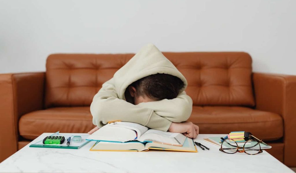 child in a hoodie sleeping on top of his books