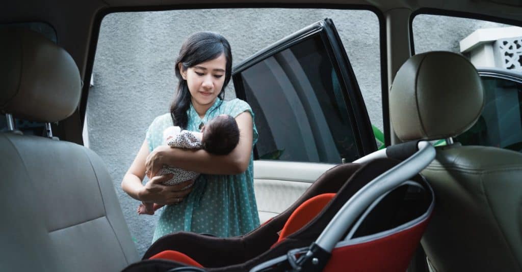 mom carrying newborn baby into a car