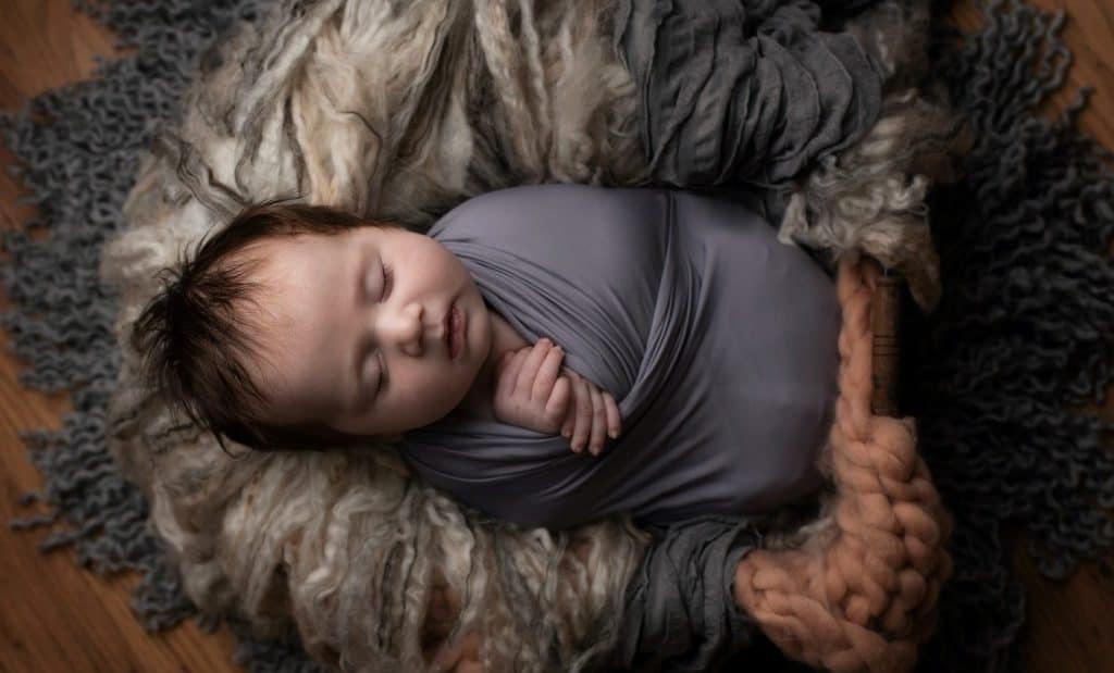 sleeping baby swaddled by gray blanket