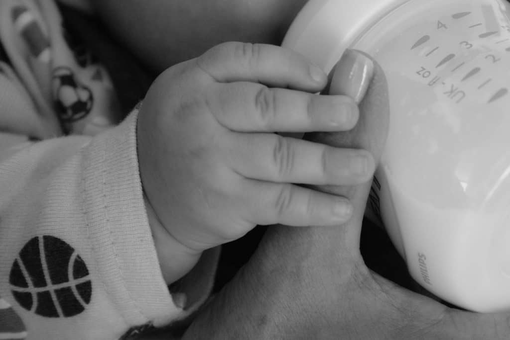 baby holding mom's hand while drinking milk
