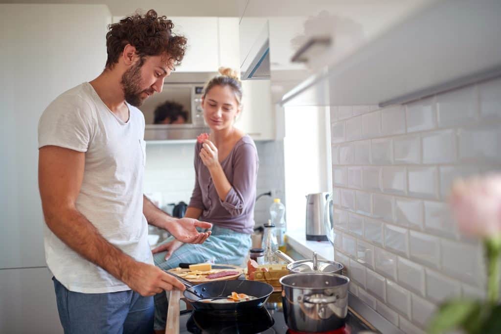 man cooking breakfast while woman sits on the kitchen