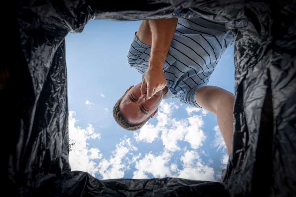 man covering his nose while looking at the trash