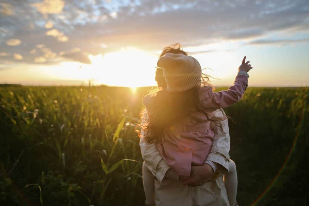 mother carrying her daughter on a grass field