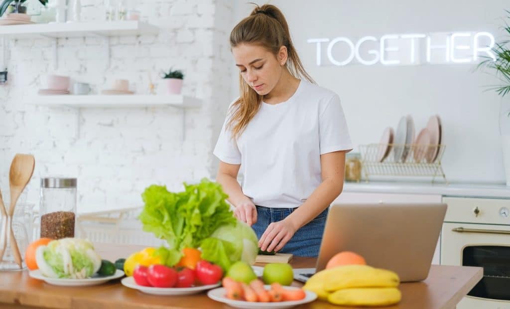 woman standing on a kitchen table filled with vegetables