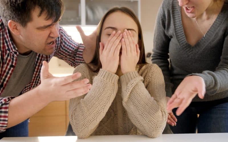 girl covering her face while parents scold her