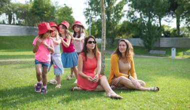 two woman sitting on a grass field while kids are playing