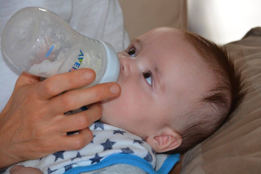 baby looking at mother while drinking milk bottle