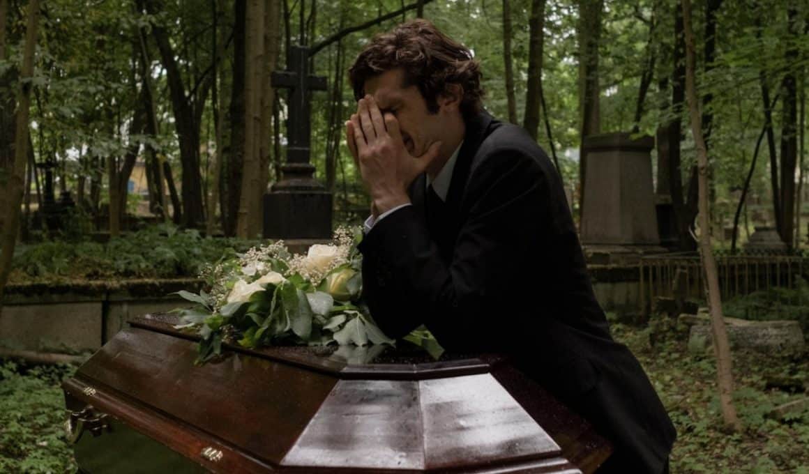 man crying beside a coffin