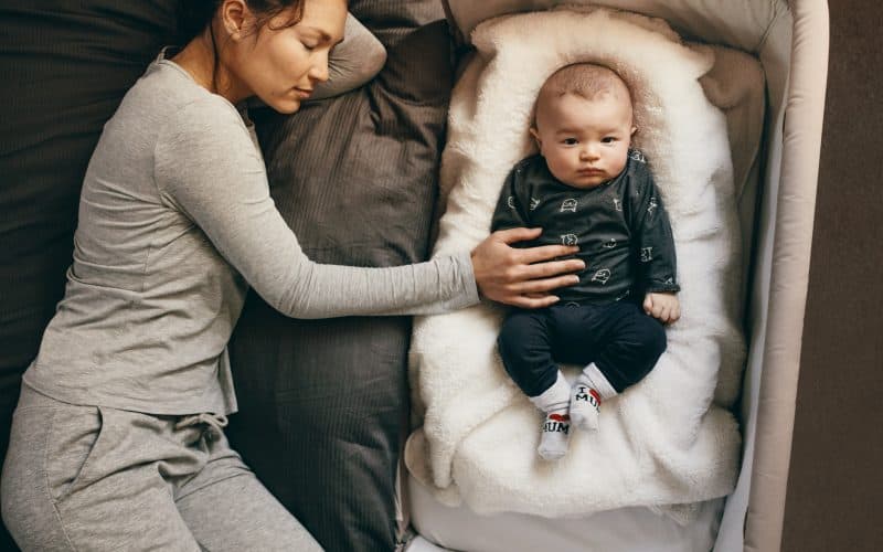 mom sleeping with baby on a bassinet