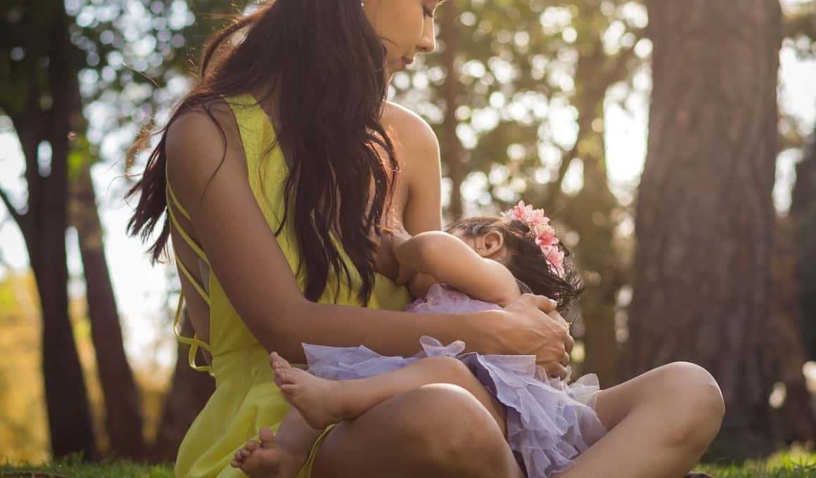 mother breastfeeding while sitting on grass