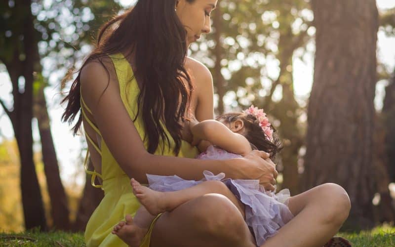 mother breastfeeding while sitting on grass