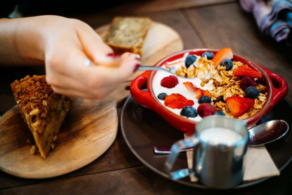 person holding spoon and ceramic fruit bowl