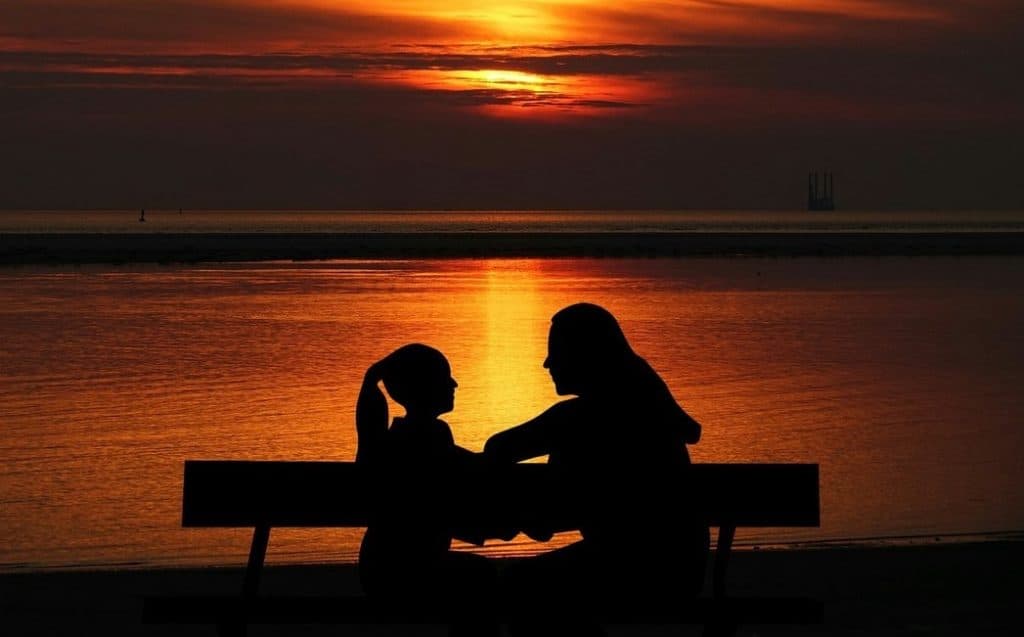 silhoutte of mother and daughter talking on a bench