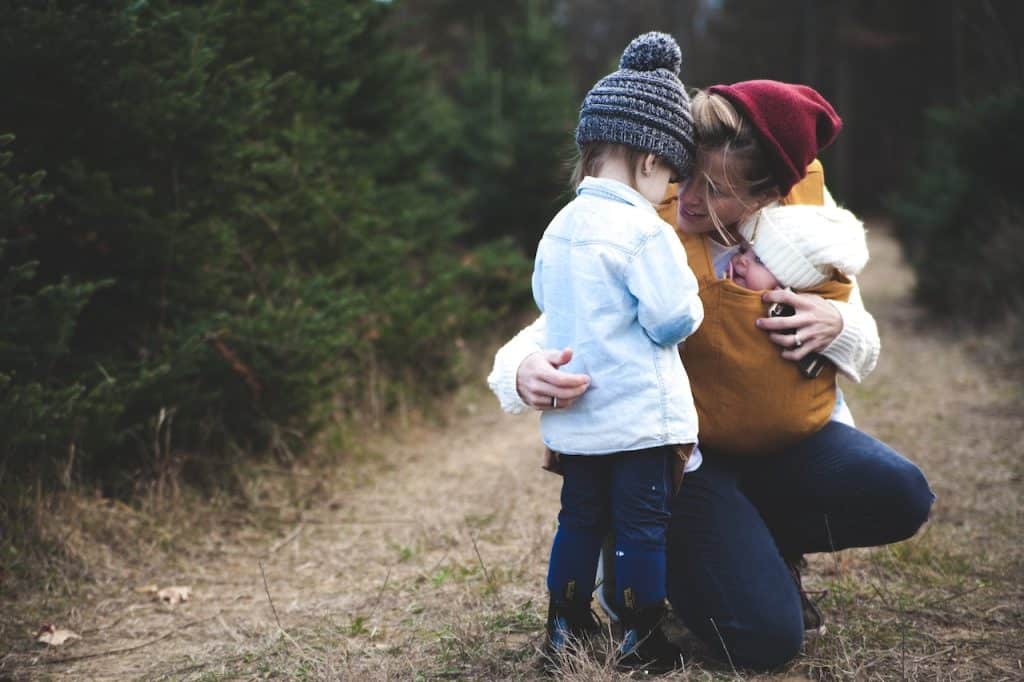 woman carrying a baby talking to her little boy