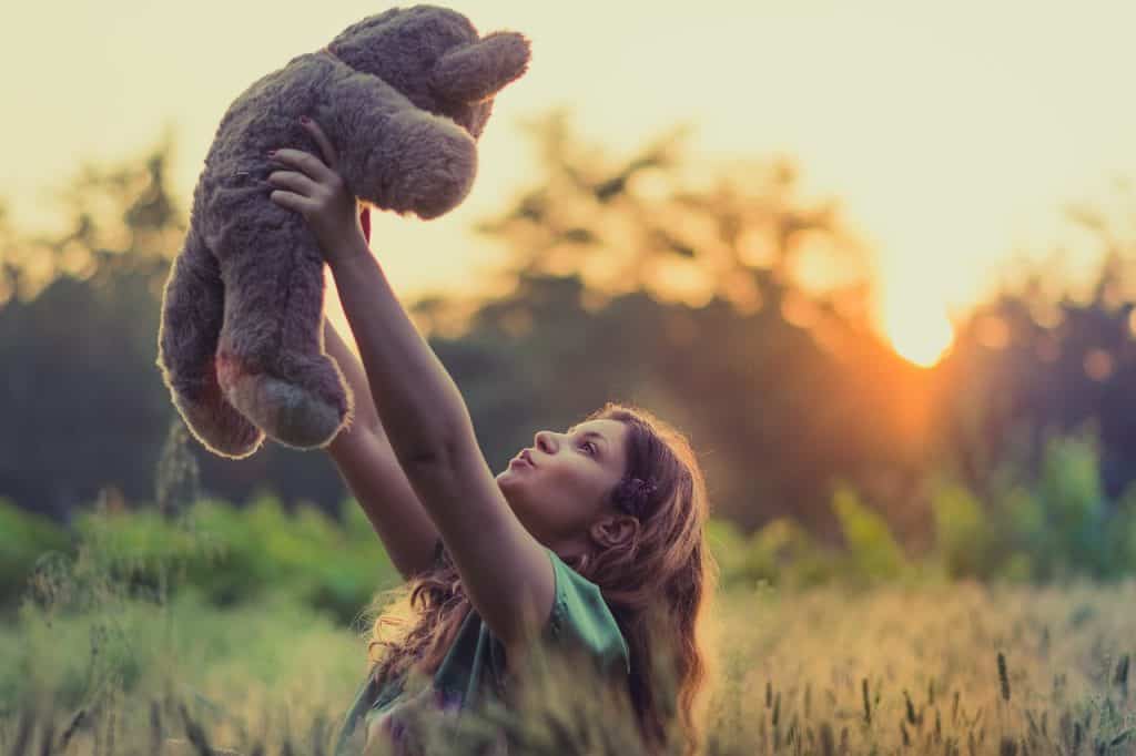girl holding teddy bear up high