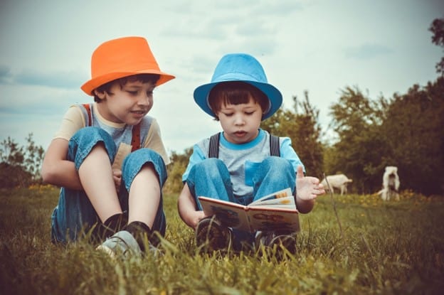 two little boys reading a book on grass