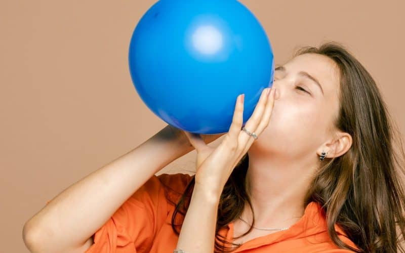 woman blowing up a blue balloon