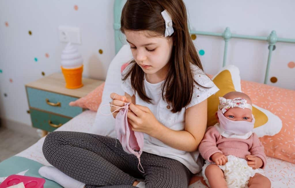 kid sewing clothes for her doll