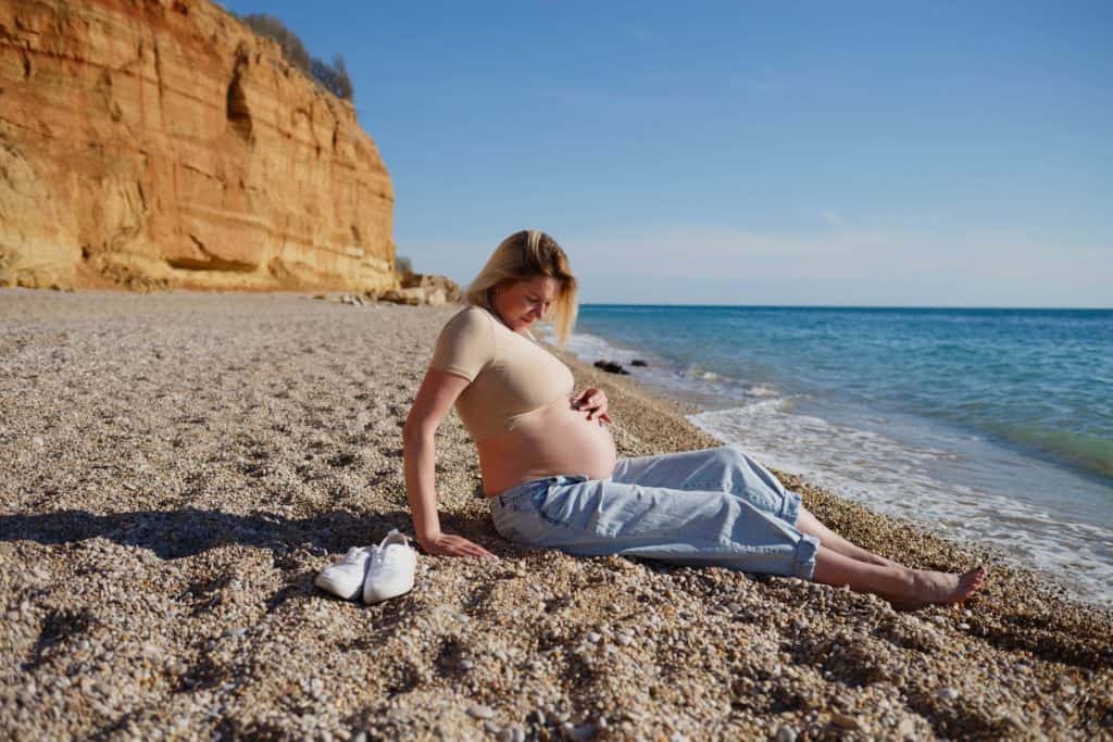 pregnant woman sitting on a shore