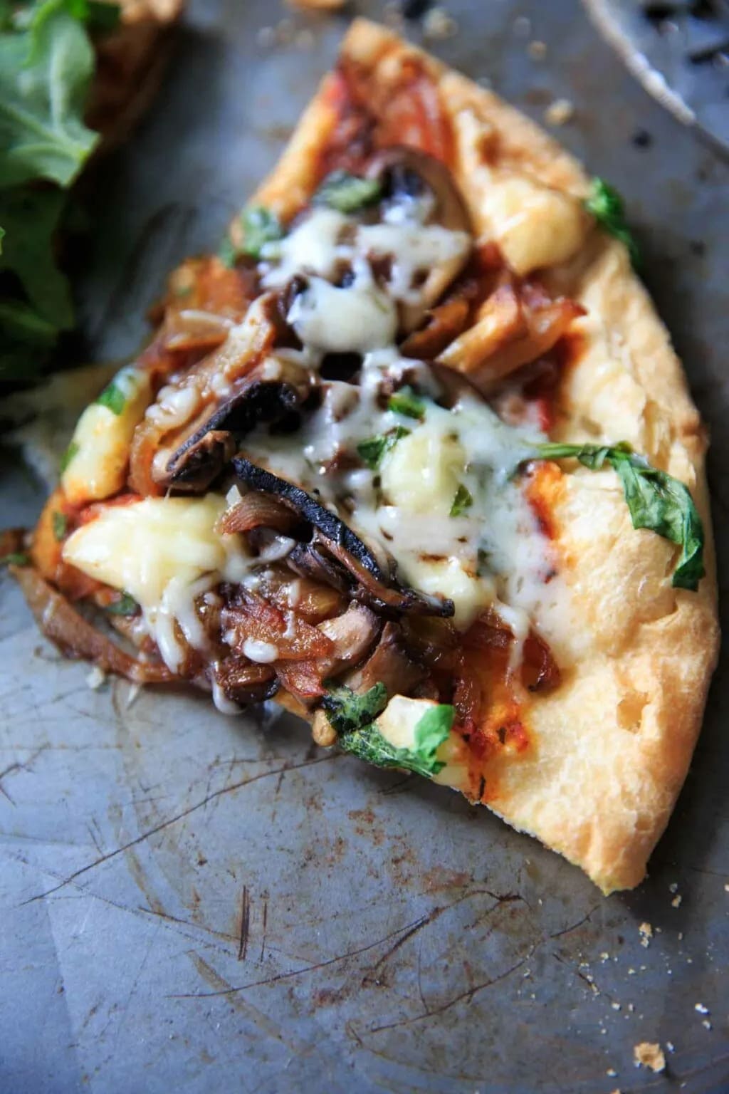 A slice of pizza with arugula, brie and caramelized onion on top.