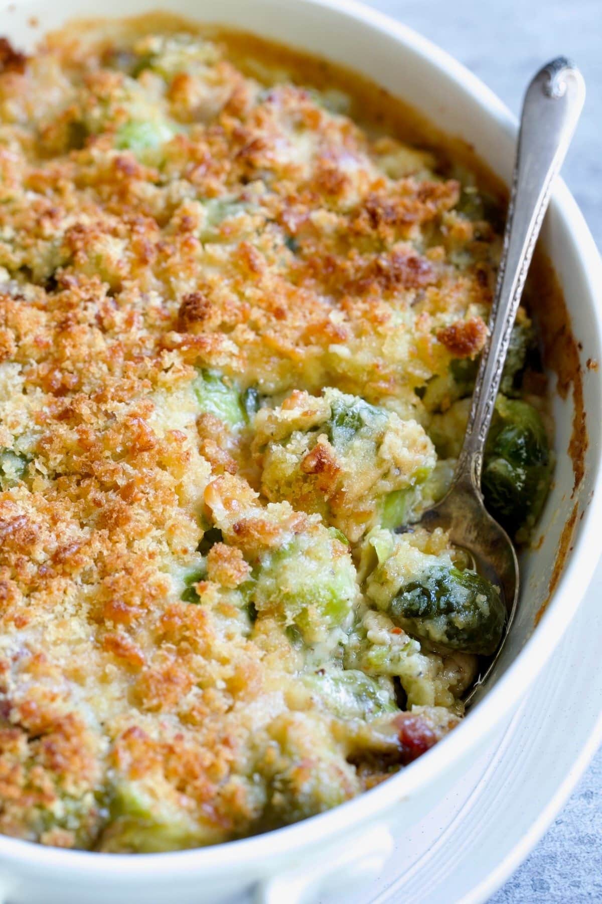 Brussels sprouts gratin with brie and bacon on a white dish.