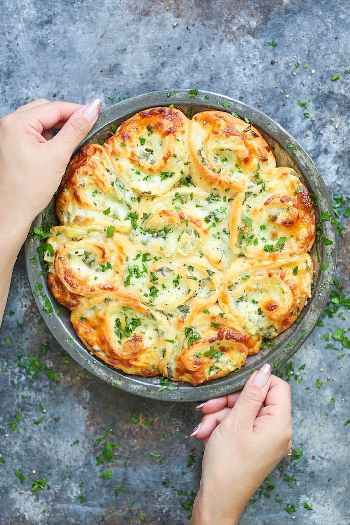 cheesy-spinach-and-artichoke-pinwheels A Woman's Hand Holding a Pan of Spinach and Artichoke Pinwheels Ready to Serve