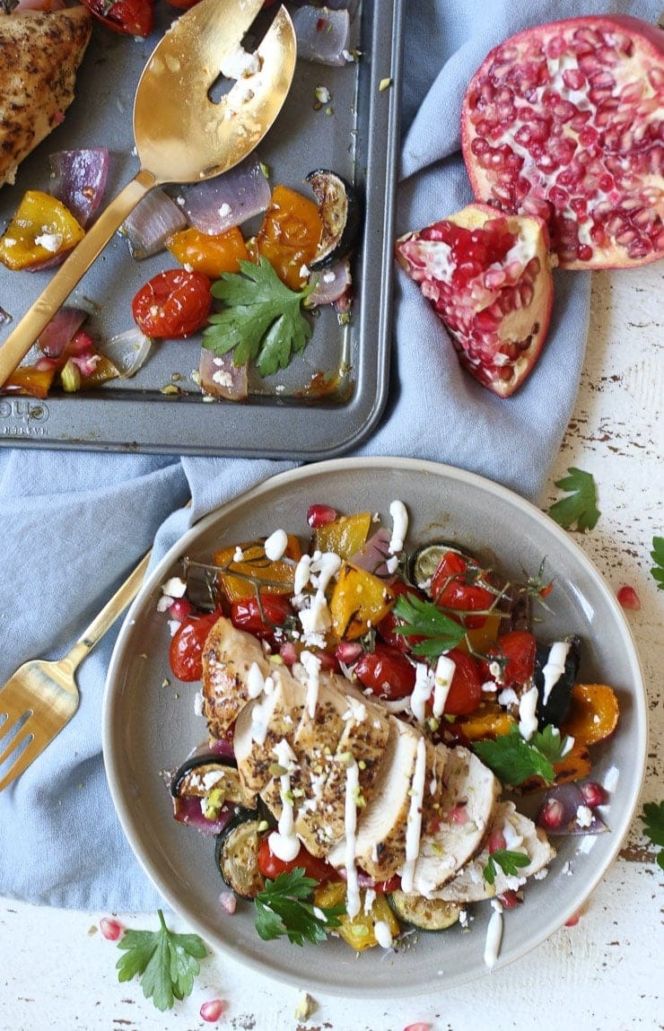 Plate with chicken cooked in a sheet pan served with sautéed vegetables on sides drizzled with white sauce.