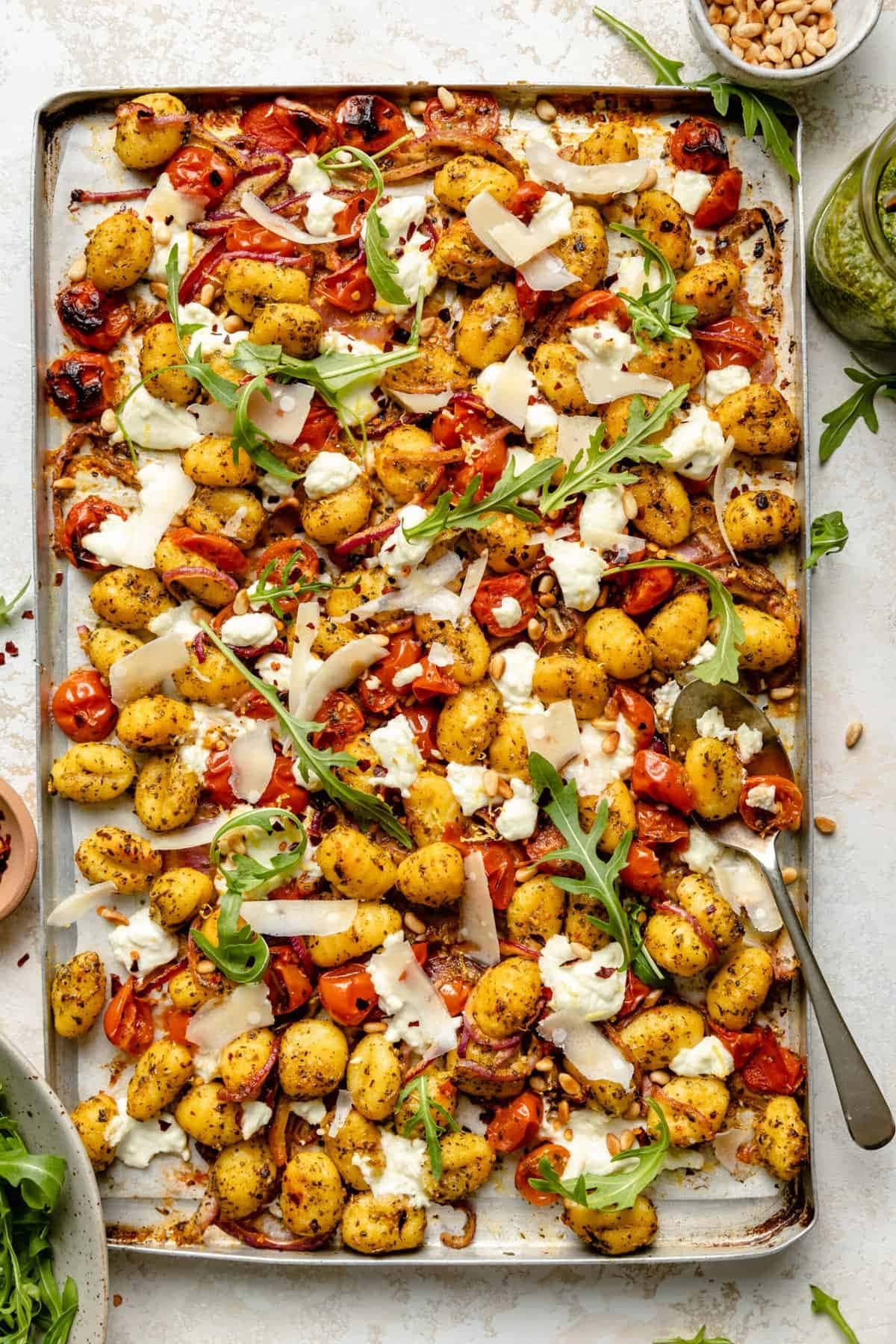 Pesto gnocchi with tomato, onions, and parmesan cheese cooked in a sheet pan.