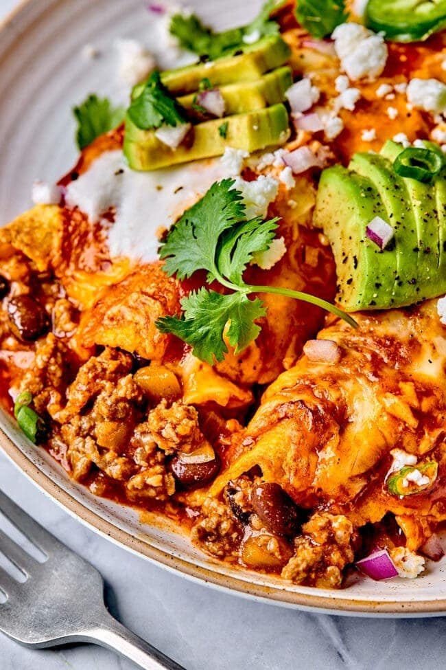 beef-enchilladas Beef enchiladas served on a plate topped with sliced avocado and cheese.
