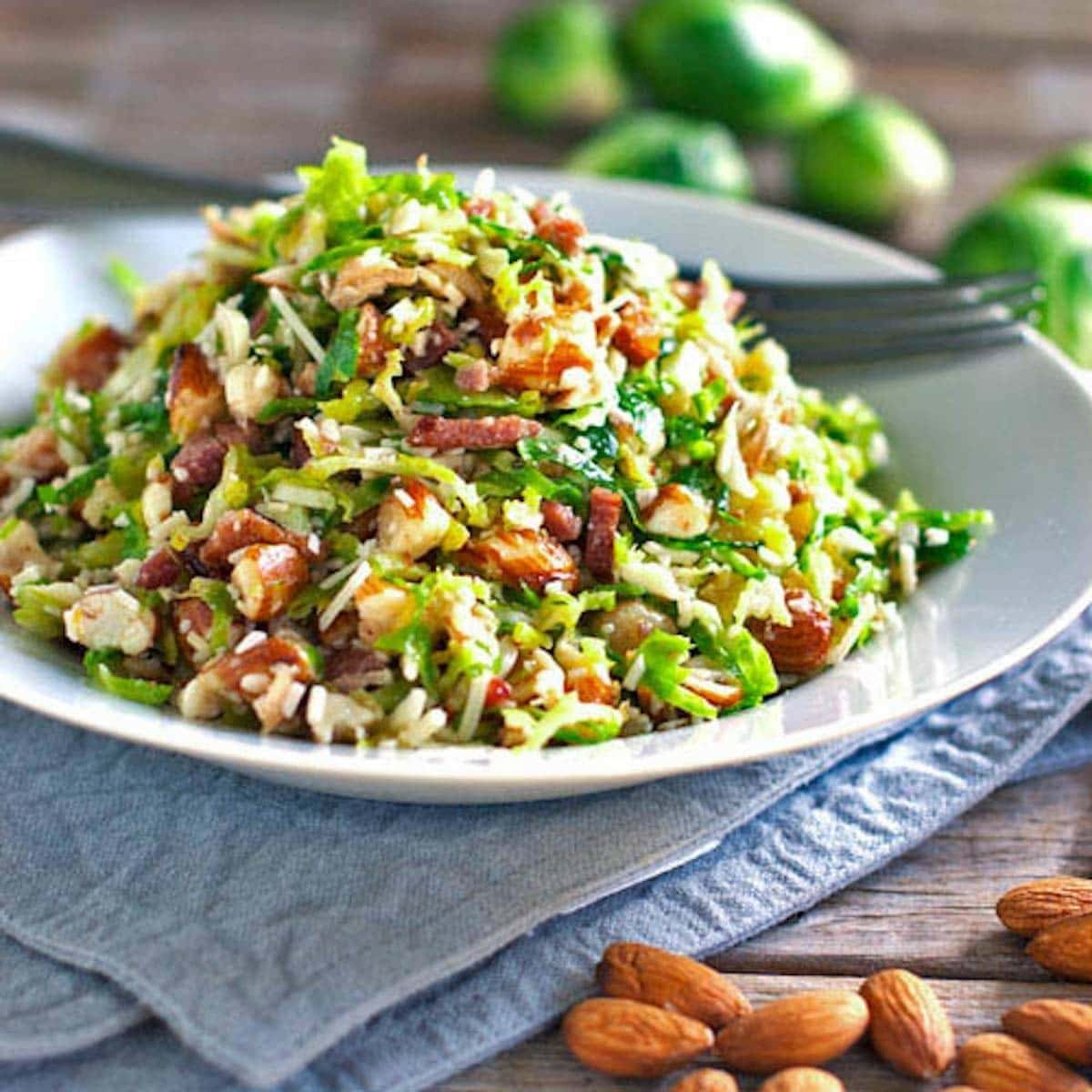 brussel-sprout-salad Bacon and brussels sprout salad with crumbled bacon, parmesan cheese and almonds served on a plate.