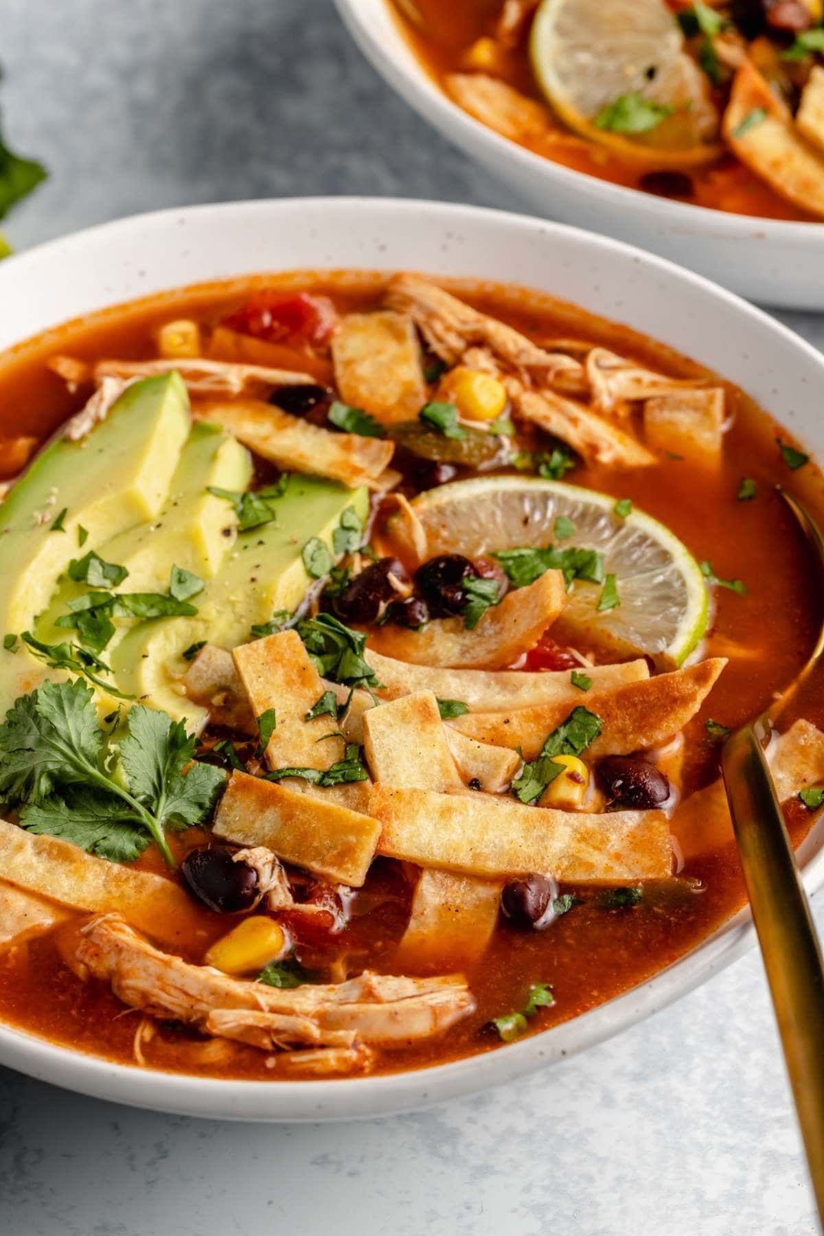 Bowl of homemade Crockpot Chicken Tortilla Soup garnished with sliced avocado, lemon and cilantro
