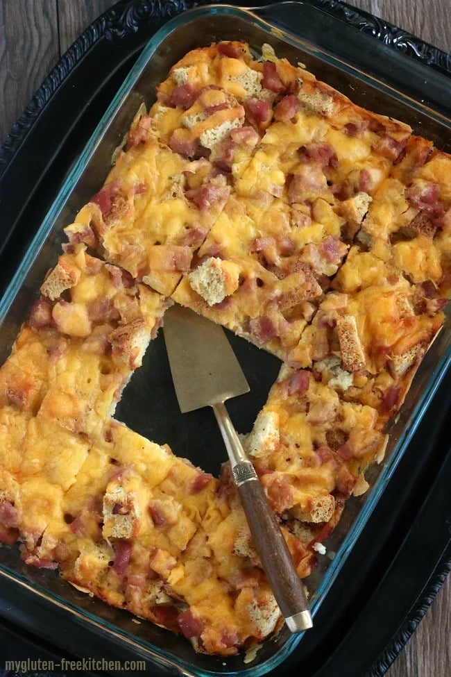gluten-free-overnight-breakfast Sliced Gluten-free overnight holiday breakfast casserole on a glass dish made with bread cubes and cheese.