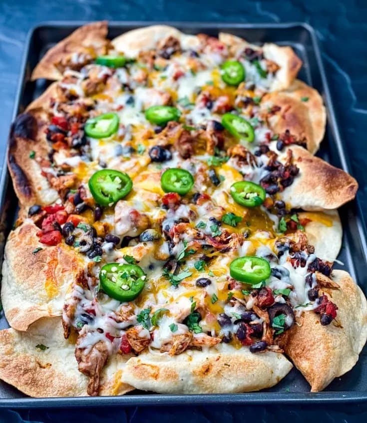 Nachos with turkey, tomatoes, onions, olives, chiles, cream and cheese filling arranged on a pan.